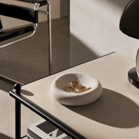 Jesmonite jewelry dish with rings on a table next to a book and chair.